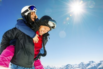Happy young caucasian skiers couple in love having fun together playing in mountains piggybacking