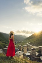 Young pretty Woman traveler in red dress looking at medieval towers of Ushguli Georgia during
