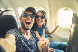 Smiling couple taking selfie inside airplane during flight, showing joy, freedom and travel