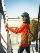 Young happy caucasian female traveler backpacker with carry on hiking backpack boarding airplane