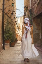 Traveler woman in white dress walking through narrow stone alley in historic city of Mardin Turkey