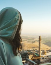 Smiling woman traveler in abaya standing above Mardin Turkey with panoramic view of Mesopotamian