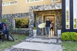 Two men leaving a house with their surfboards