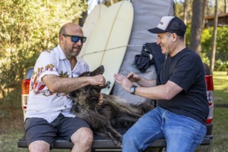 Two men and their dog relaxing on a pickup truck