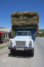A blue lorry loaded with several layers of hay bales is parked on a country road, Armenia