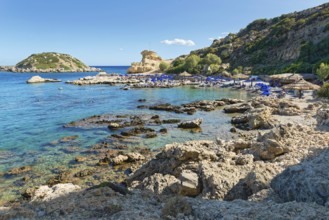 Grande Blue rocky beach with blue sea, umbrellas and surrounding cliffs under clear skies, Grande