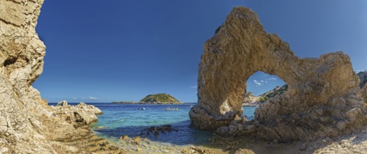 Stone arch on Grande Blue Beach in front of a small island and a rocky coastline under a clear blue