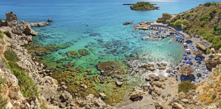 Secluded Grande Blue Bay with clear turquoise water and rocks, along which a row of beach loungers