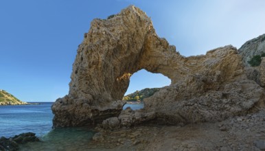 Rock arch at Grande Blue Beach under a clear blue sky in a sunny coastal landscape, Grande Blue