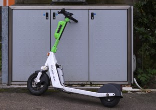 On the pavement, pavement, container for waste bins, parked e-scooter, electric scooter, scooter,
