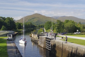 A sailing boat in the canal surrounded by green trees and mountains on a clear day, Caledonian
