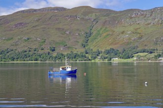 Small boat floating on a calm lake surrounded by green mountains, Fort William, Scotland, United