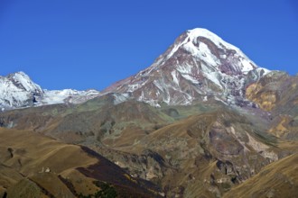 The snow- and ice-covered summit of Kasbek, with the Gergetier Trinity Church at the bottom left,