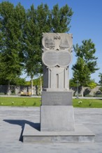 Stone monument with inscription in front of tall trees, in the garden of the Yazidi temple, Yazidi