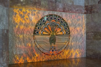 Detailed peacock pattern on a wall with orange lighting, showing symbolism and artistic decoration,