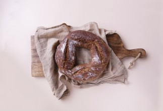 Round handmade rye bread on wooden board with linen napkin, on beige background top view, copy