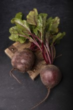 Beetroot with tops lies on a wooden board on a dark background, selective focus