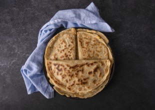 Appetizing pancakes with filling on a plate with a blue napkin, on a black background, space for