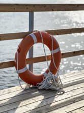 Orange lifebuoy stands on wooden pier, copy space