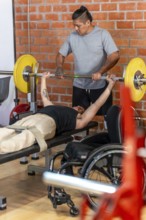 Adaptive athlete in a wheelchair performing bench press exercises with a spotter at the gym,