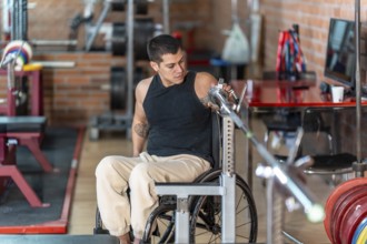 Disabled man in a wheelchair performing weight training with a barbell at a gym, focusing on