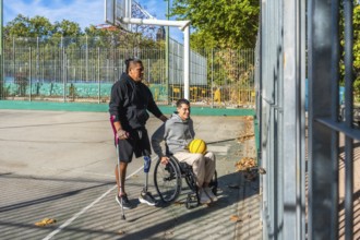 Friends celebrating sports inclusion on a sunny outdoor basketball court, one man with crutches and