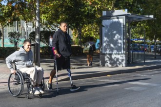 Two amputee men, one using a wheelchair and the other a prosthetic leg with crutch, navigating an