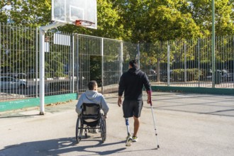 Two young men, one in a wheelchair and the other with a prosthetic leg, are walking together