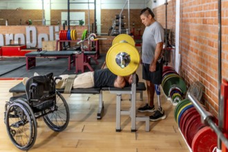 Two determined men training in a gymone bench pressing weights while his teammate with a prosthetic