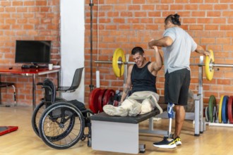 Two physically challenged men exercising together, one using a wheelchair for support on a bench