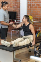 Two men shaking hands in a gym as a trainer supports an adaptive athlete with a prosthetic leg and