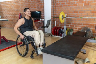 Young man in a wheelchair preparing for a workout next to a weightlifting bench and barbell at an