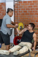 Two adult disabled men training together at a gym, one with a prosthetic leg helping the other, who