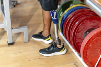 Amputee man standing on a wooden floor in a gym, wearing a modern prosthetic leg and a normal shoe