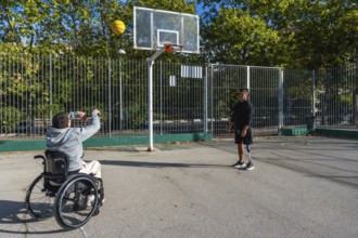 Two disabled friends are enjoying a game of basketball on an outdoor court, with one man in a