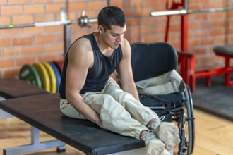 Young man with a prosthetic leg sitting on a weight bench, focusing on his leg during a workout