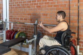 Young man in a wheelchair setting up a barbell in a modern gym, focused and determined as he trains