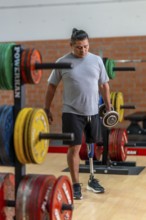 Man with prosthetic leg training at the gym, carrying heavy weights, demonstrating strength,