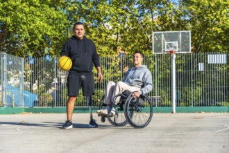 Two young men, one with a prosthetic leg holding a basketball and another sitting in a wheelchair,