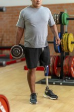Disabled man with prosthetic leg lifting a dumbbell in gym, focused on strength training and