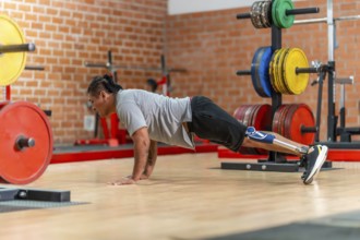 Athlete with a prosthetic leg doing push ups on a gym floor, showing determination, adaptive