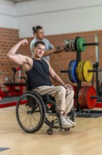 Adaptive athlete in a wheelchair flexing his bicep and smiling while a trainer adjusts weight