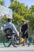 Men with a wheelchair and a prosthetic leg are happily dribbling a yellow basketball on an outdoor