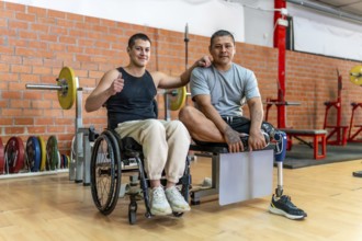 Two adaptive athletes standing together in a gym, one man uses a wheelchair and the other has a