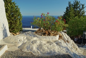 Sunny square with blooming oleander, surrounded by white rocks and views of the blue sea, Church of