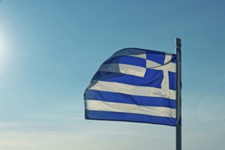 The Greek flag flies in the wind against a clear blue sky with sunshine, Church of the Virgin Mary