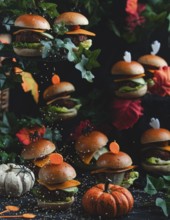 Sesame seeds trickle onto small burgers and pumpkins in a Halloween atmosphere