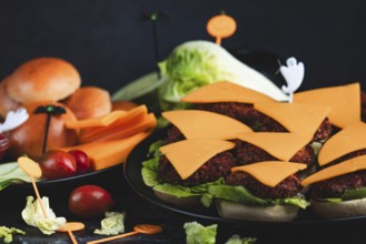 Topped burger buns with cheese, salad and Halloween decoration