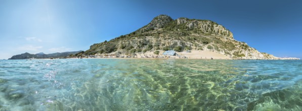 Picturesque Tsambika beach with clear water and rocky mountain landscape under a blue sky, Tsambika