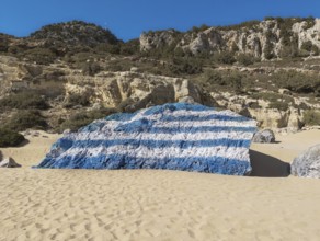 Rock painted with a Greek flag on the sandy Tsambika beach under a clear sky, Tsambika beach,